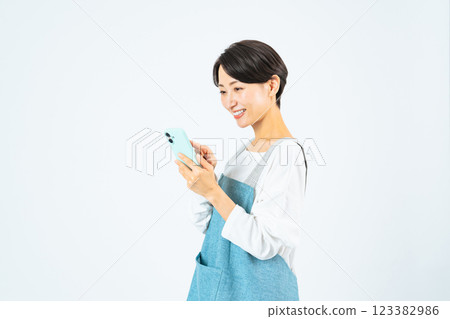 一名身穿圍裙的中年婦女帶著微笑使用智慧型手機 123382986