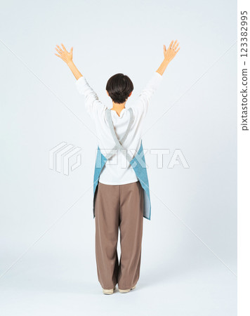 Full-body photo of a woman wearing an apron raising her arms in the air Full-body photo of a woman wearing an apron raising her arms in the air 123382995
