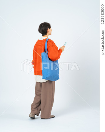 一位時尚中年女性拿著智慧型手機行走的全身照片 123383000