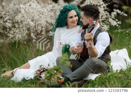 a bearded groom plays a stringed instrument and a girl sits in a spring meadow 123383796