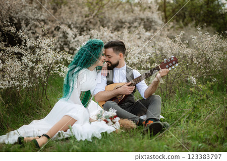 a bearded groom plays a stringed instrument and a girl sits in a spring meadow 123383797