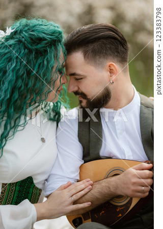a bearded groom plays a stringed instrument and a girl sits in a spring meadow 123383798