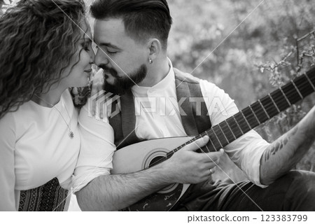 a bearded groom plays a stringed instrument and a girl sits in a spring meadow 123383799
