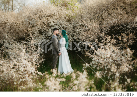 a bearded groom plays and a girl with green hair against the background of blooming spring 123383819