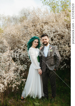 a bearded groom plays and a girl with green hair against the background of blooming spring 123383820