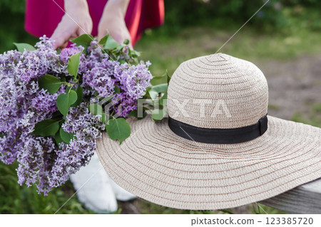 Close-up view of vibrant lilac flowers paired with a classic straw hat in a serene, green environment. The image conveys elegance, tranquility, and the beauty of nature during springtime. Close-up view of vibrant lilac flowers paired with a classic straw hat in a serene, green environment. The image conveys elegance, tranquility, and the beauty of nature during springtime. 123385720