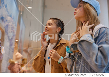 Happy teenage girls friends looking through showcase window in shopping mall Happy teenage girls friends looking through showcase window in shopping mall 123385979