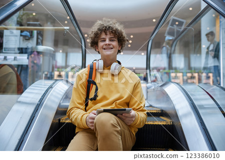 Trendy teenage boy posing on stopped escalator staircase in shopping mall 123386010