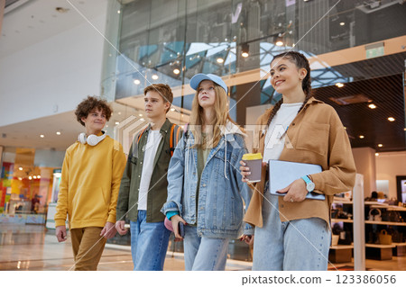Relaxed teenage friends sitting on bench of big shopping city center Relaxed teenage friends sitting on bench of big shopping city center 123386056