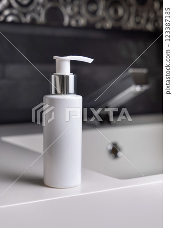 White cream bottle near modern faucet on basin in dark grey bathroom close up, cosmetic mockup White cream bottle near modern faucet on basin in dark grey bathroom close up, cosmetic mockup 123387185