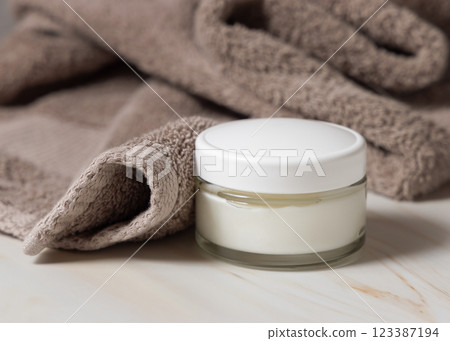Cream jar near with white lid light brown bath towel closeup, Natural organic cosmetics for facial care Cream jar near with white lid light brown bath towel closeup, Natural organic cosmetics for facial care 123387194