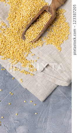Raw uncooked yellow millet grain in a wooden spoon on grey table, top view. Ancient food 123387205