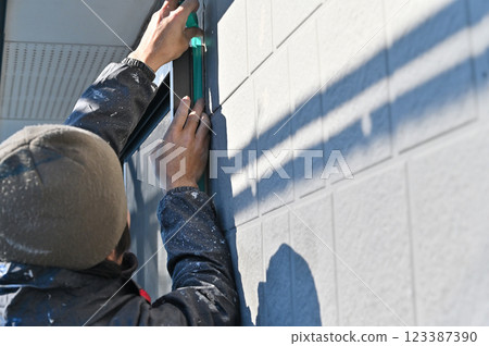 A craftsman masking a wall, replacing caulking, exterior wall painting work A craftsman masking a wall, replacing caulking, exterior wall painting work 123387390