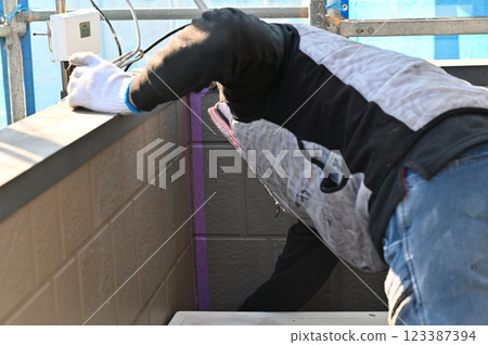 A craftsman masking a wall, replacing caulking, exterior wall painting work A craftsman masking a wall, replacing caulking, exterior wall painting work 123387394