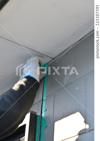 A craftsman masking a wall, replacing caulking, exterior wall painting work A craftsman masking a wall, replacing caulking, exterior wall painting work 123387395