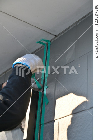 A craftsman masking a wall, replacing caulking, exterior wall painting work 123387396