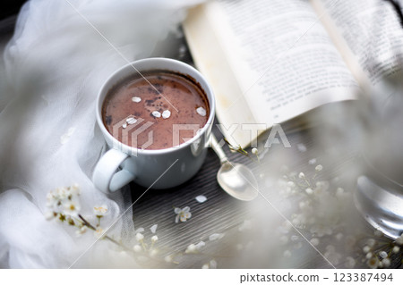 Cup of aromatic hot chocolate with book and cherry flowers Cup of aromatic hot chocolate with book and cherry flowers 123387494