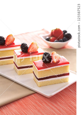 Sweet and colorful layered cakes with a glossy red topping, fresh strawberries, and blackberries. The soft sponge, creamy layers, and fruity flavors make it a tasty dessert. Sweet and colorful layered cakes with a glossy red topping, fresh strawberries, and blackberries. The soft sponge, creamy layers, and fruity flavors make it a tasty dessert. 123387523