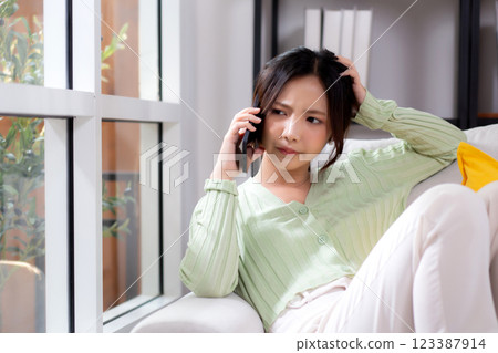 Asian young woman stress and worried sitting on sofa while speaking on smart phone in living room. 123387914