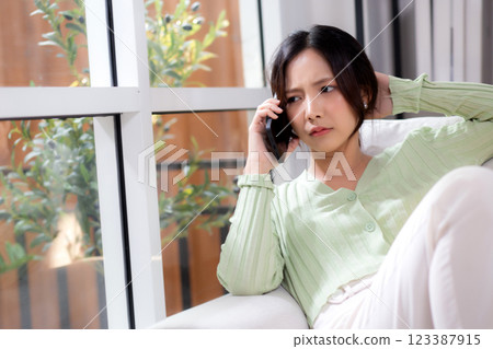 Asian young woman stress and worried sitting on sofa while speaking on smart phone in living room. 123387915