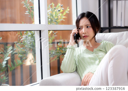 Asian young woman stress and worried sitting on sofa while speaking on smart phone in living room. Asian young woman stress and worried sitting on sofa while speaking on smart phone in living room. 123387916