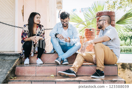 Three teenage friends talking sitting on the stairs, Three young people sitting on the street talking. Concept of friends talking, Three young friends talking sitting on the stairs 123388039