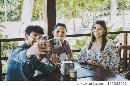 Young friends taking a selfie in a coffee shop. Three happy people in a coffee shop taking a selfie. Front view of teenage friends taking selfie and having fun in a cafe restaurant 123388212