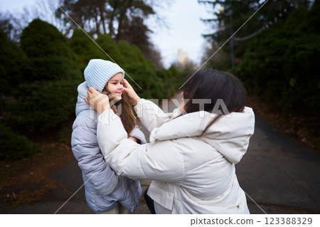 Mother helps daughter with hat on a cool day in a park setting 123388329
