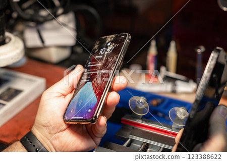 A technician is inspecting a smartphone with a cracked screen at a bustling phone repair service during the day. A technician is inspecting a smartphone with a cracked screen at a bustling phone repair service during the day. 123388622