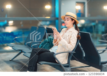 Young Caucasian elegant woman is sitting in lounge chair at airport waiting room and using smartphone. Concept of travel app Young Caucasian elegant woman is sitting in lounge chair at airport waiting room and using smartphone. Concept of travel app 123390834