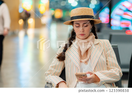 Portrait of young Caucasian elegant woman is sitting in an airport lounge chair and holds smartphone. Concept of flight app 123390838
