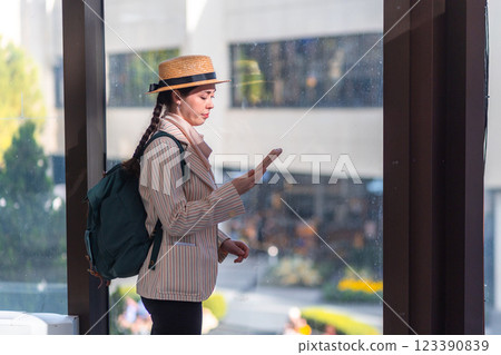 Side view of a young Caucasian elegant woman in a straw hat and jacket, using a smartphone. near big windows in the airport. Concept of app for trip and flight Side view of a young Caucasian elegant woman in a straw hat and jacket, using a smartphone. near big windows in the airport. Concept of app for trip and flight 123390839