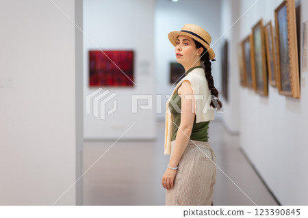 Mid shot of young Caucasian woman in a straw hat and elegant clothes visits a contemporary art gallery. Copy space 123390845