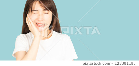 Asian woman suffering from toothache or jaw pain over blue background. Cause of painful included tooth decay, inflammation, dental abscess, gum disease, sensitive teeth or trigeminal neuralgia. Asian woman suffering from toothache or jaw pain over blue background. Cause of painful included tooth decay, inflammation, dental abscess, gum disease, sensitive teeth or trigeminal neuralgia. 123391193