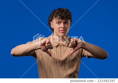 Young curly haired man with sign of dislike. Guy shaming, expressing thumbs-down Young curly haired man with sign of dislike. Guy shaming, expressing thumbs-down 123392197