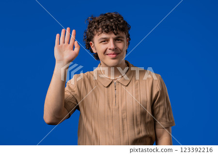 Friendly curly haired young Man Waving Hand - Hello, Hi, Salute. Greetings. 123392216