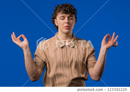 Tranquil curly man relaxing, meditating, refuses stress. Breathes deeply on blue Tranquil curly man relaxing, meditating, refuses stress. Breathes deeply on blue 123392220