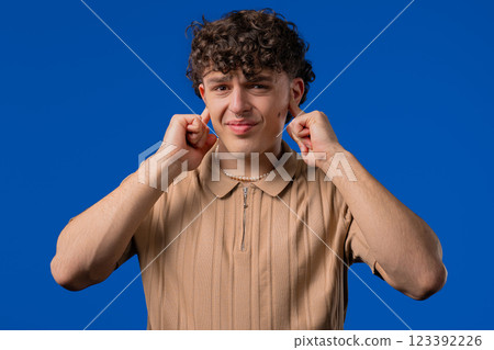 Annoyed man with shut ears on blue. Guy block annoying sounds, loud music, noise Annoyed man with shut ears on blue. Guy block annoying sounds, loud music, noise 123392226