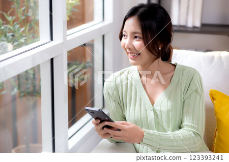 Young asian businesswoman looking smartphone smiling and relax sitting on sofa in living room. 123393241