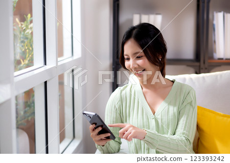 Young asian businesswoman looking smartphone smiling and relax sitting on sofa in living room. Young asian businesswoman looking smartphone smiling and relax sitting on sofa in living room. 123393242