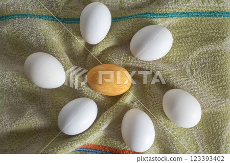 Golden egg surrounded by white eggs on a textured surface. 123393402