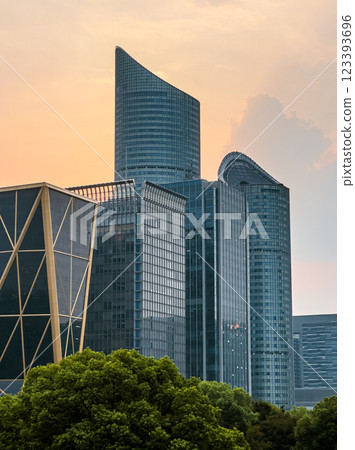 Modern skyscrapers illuminated by sunset in an urban setting near a lush green park 123393696