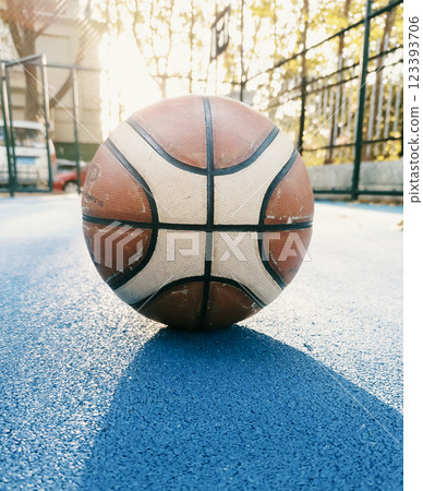 Basketball resting on a blue court during golden hour with sunlight illuminating the background Basketball resting on a blue court during golden hour with sunlight illuminating the background 123393706