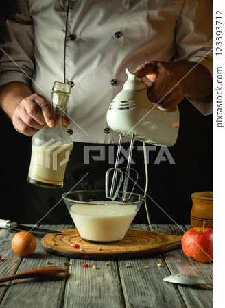 The cook preparing milkshake with fruits on kitchen table with electric hand mixer. Delicious milk recipes menu concept for breakfast. European cuisine 123393712