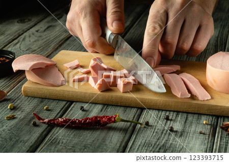 Hands skillfully chop slices of deli meat on a wooden cutting board, surrounded by vibrant spices and a red chili pepper, showcasing a love for cooking and preparation Hands skillfully chop slices of deli meat on a wooden cutting board, surrounded by vibrant spices and a red chili pepper, showcasing a love for cooking and preparation 123393715