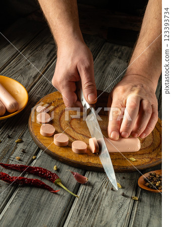 A pair of hands skillfully cut sausage into even slices on a wooden cutting board. Spices and a plate accompany the preparation, indicating a flavorful meal in progress 123393734
