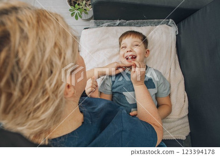 boy lying on soft black sofa during speech therapy session with female therapist in cozy room, concept of speech correction, childhood development, and healthcare 123394178