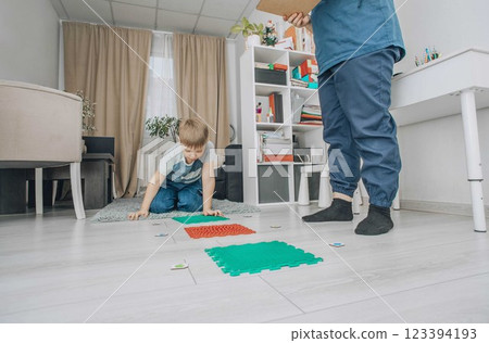 boy ready for balancing on sensory mat while reaching for a card, session in bright room with therapist, concept of motor skill development, rehabilitation, pediatric physiotherapy 123394193