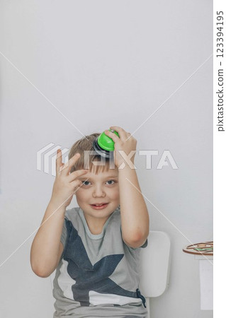boy in therapy room with green bell balanced on his head. he clasps his hands and smiles, concept of childhood education, cognitive development boy in therapy room with green bell balanced on his head. he clasps his hands and smiles, concept of childhood education, cognitive development 123394195