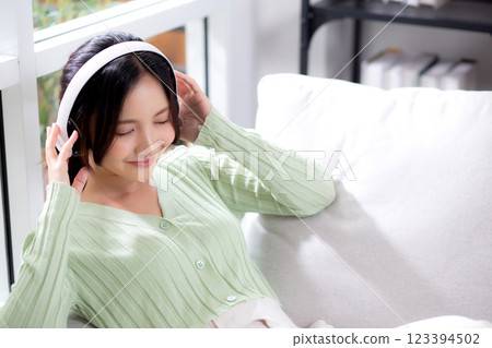 Happy young asian woman wearing headphones listening music while sitting on sofa with fun. Happy young asian woman wearing headphones listening music while sitting on sofa with fun. 123394502